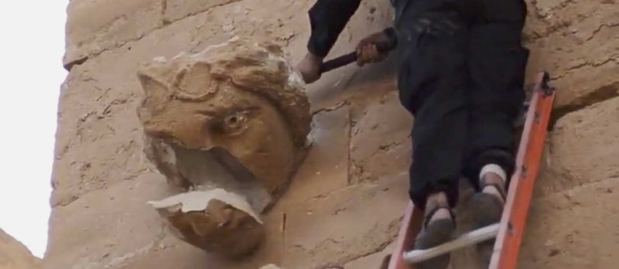 Em imagem retirada do vídeo divulgado pelo Estado Islâmico, jihadista em escada destrói escultura com golpes de marreta (Foto: Uncredited / AP)